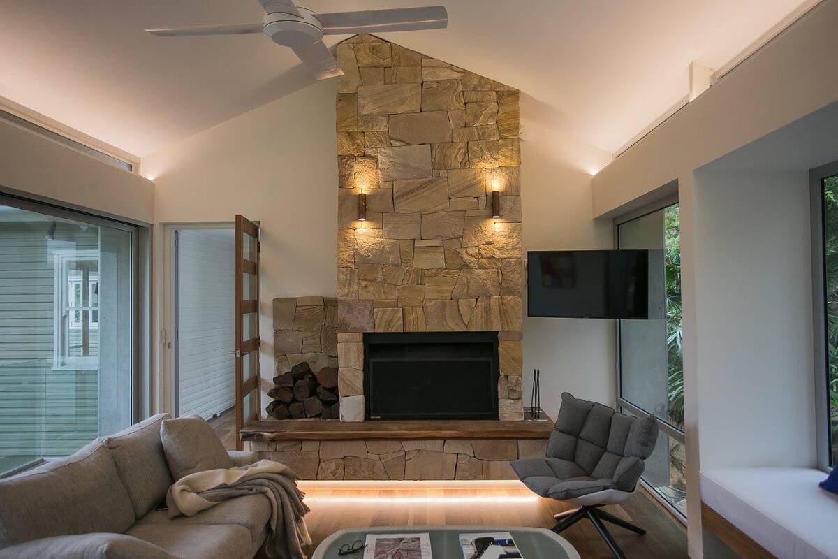Sandstone fireplace with timber mantel, wall lights and log store in a bright Bilgola Beach living room