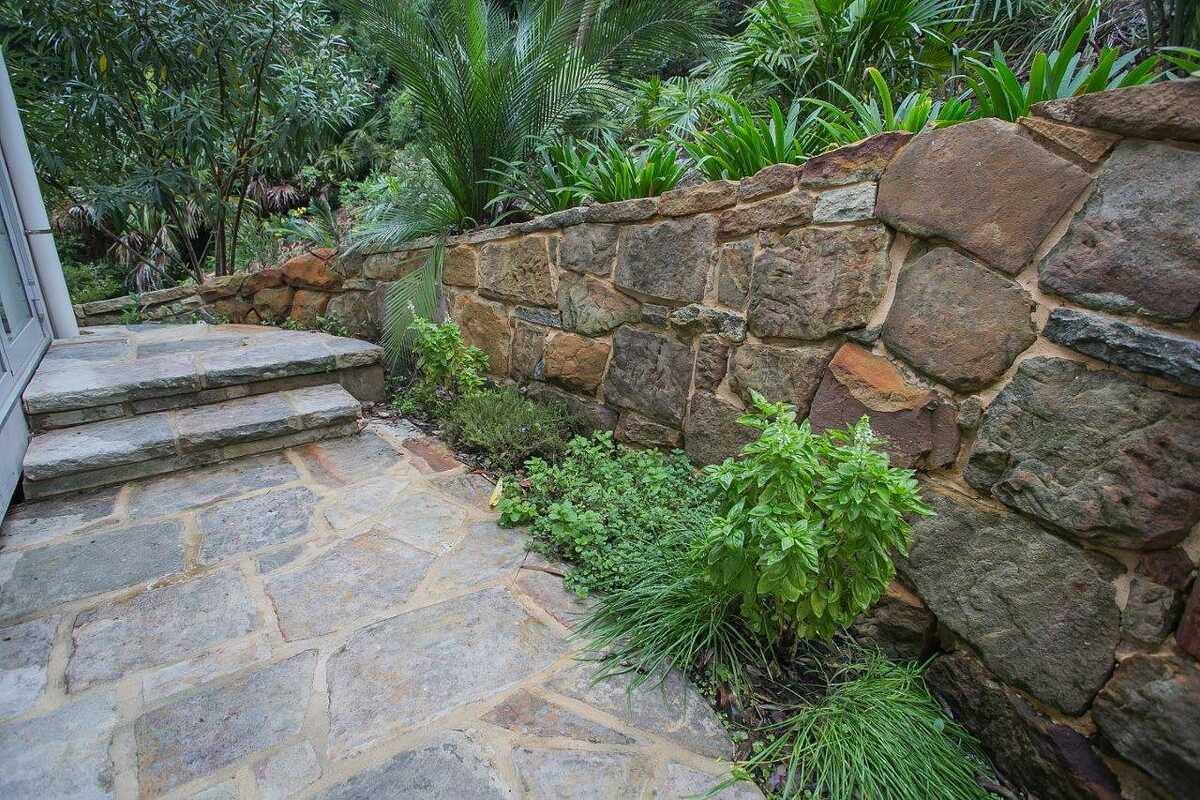 Weathered sandstone rubble wall above a crazy-paved path and tropical garden at Bilgola Beach