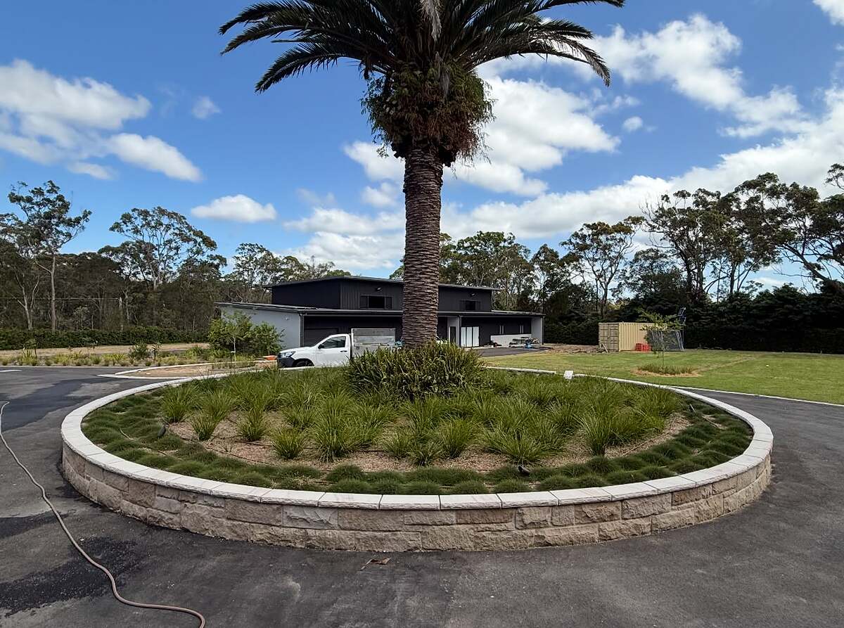 Circular sandstone block planter wall with palm tree in a driveway turning circle