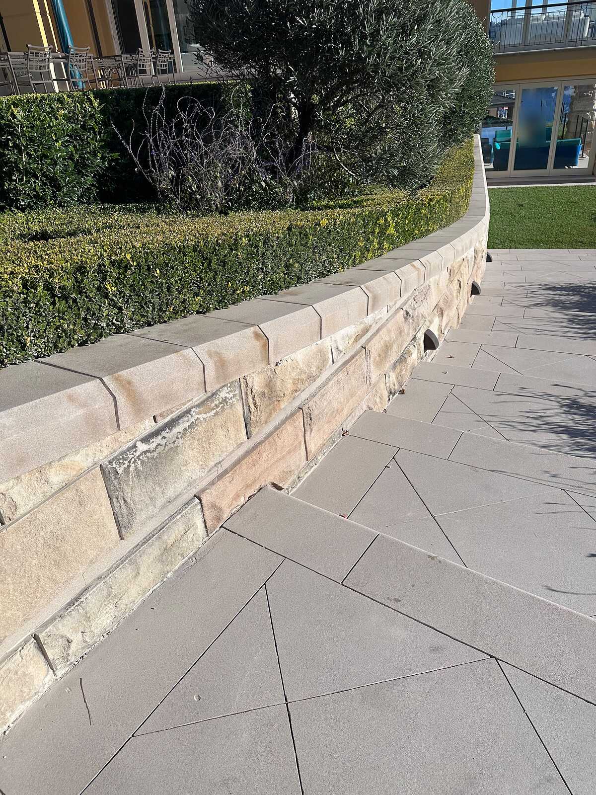 Curved sandstone garden wall with sawn coping beside large-format grey stone paving