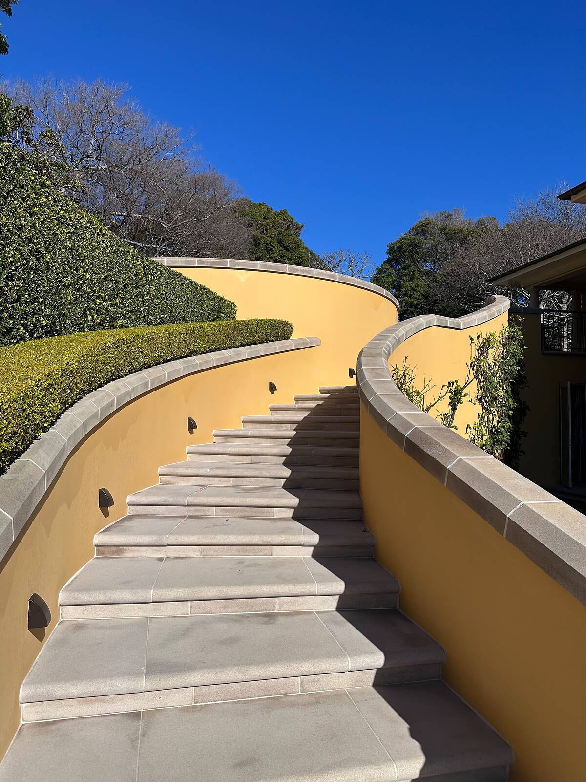 Sweeping curved staircase of sawn sandstone treads between rendered walls with sandstone coping