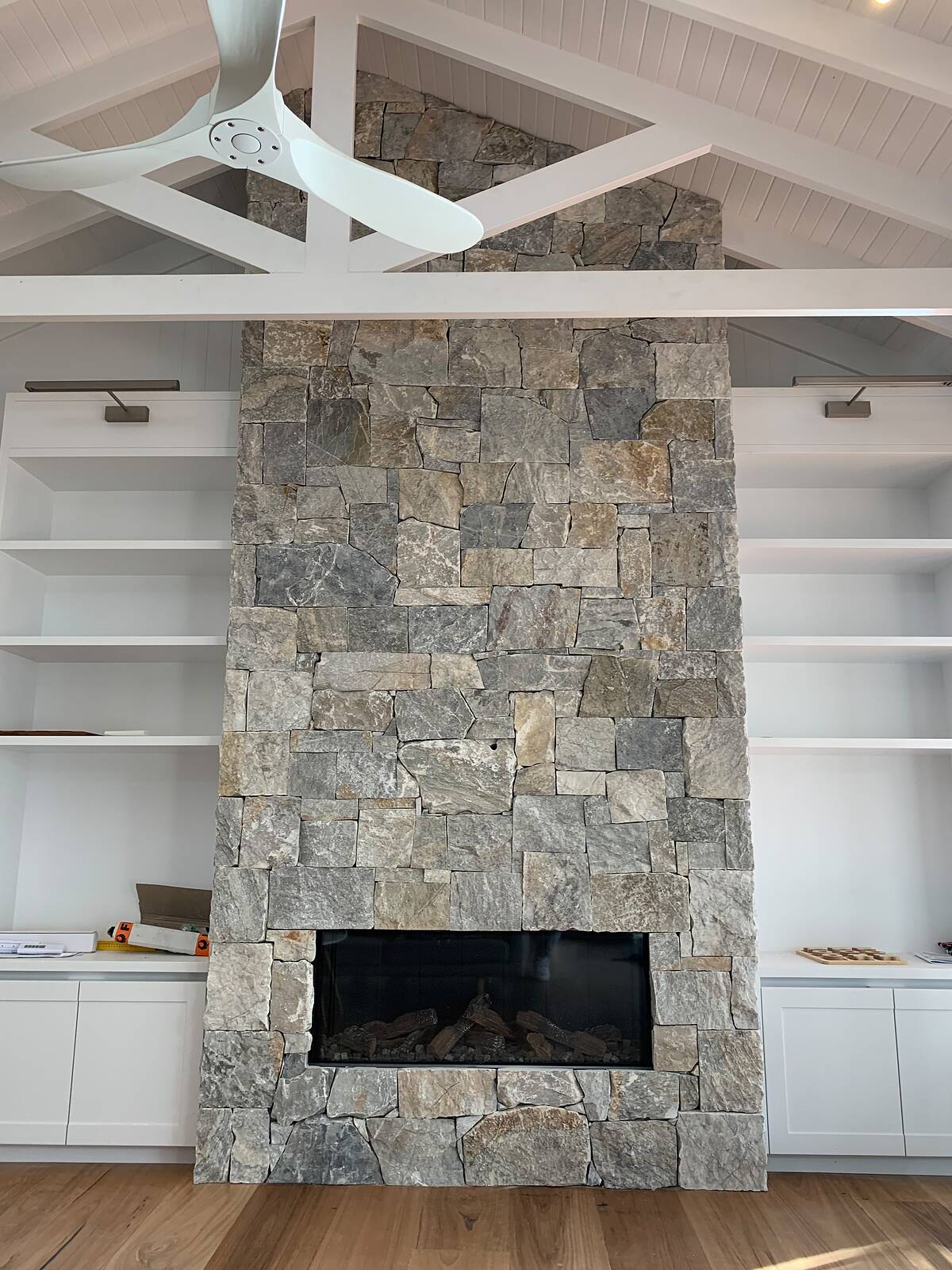 Full-height grey stone fireplace with linear gas fire beneath a raked white timber ceiling