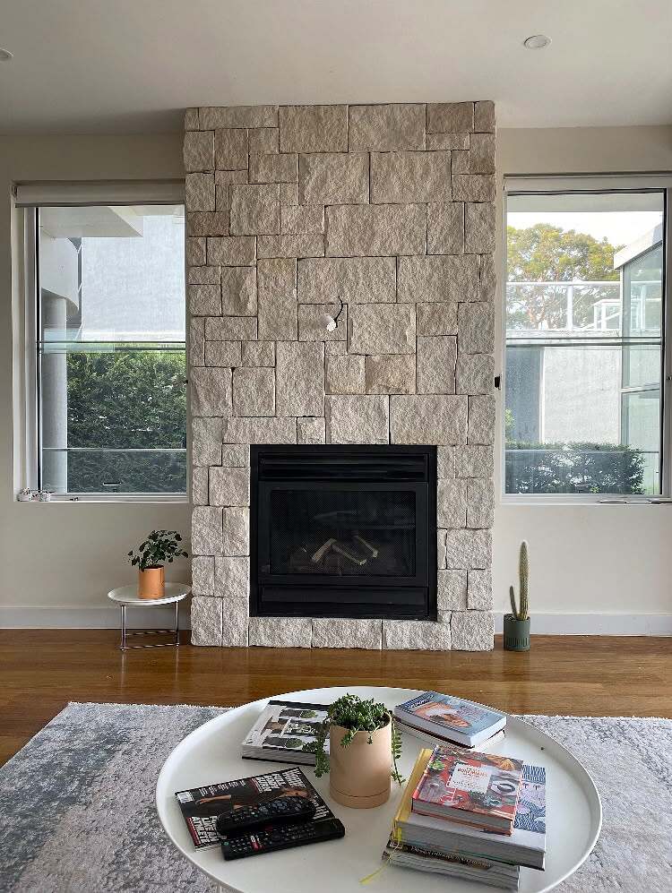 Light split-face limestone gas fireplace surround between two windows