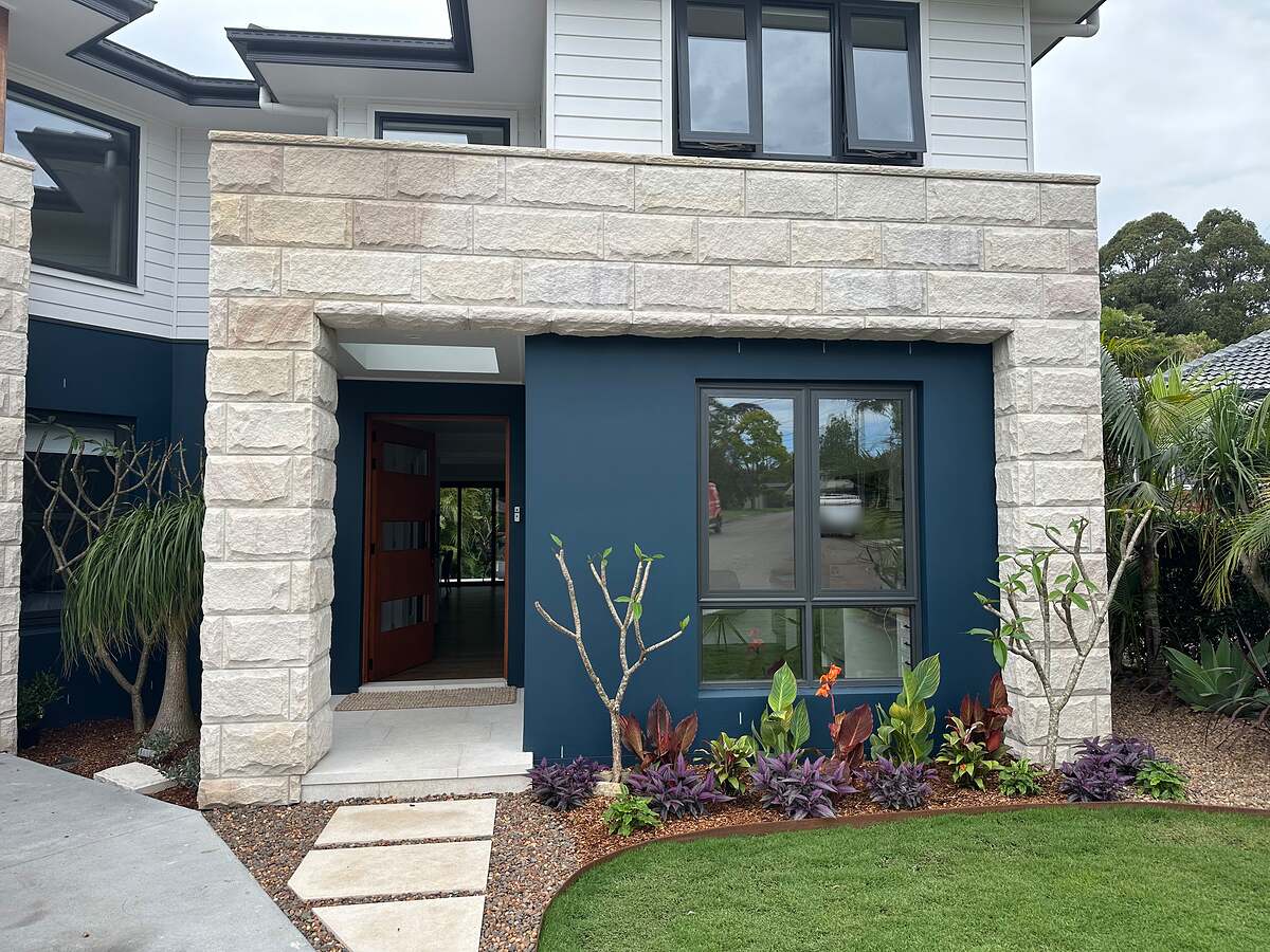 Light split-face stone cladding framing a navy-blue entry on a modern two-storey home