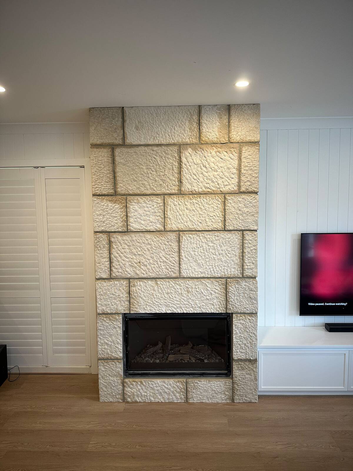 Fireplace chimney clad in large pitched-face light stone blocks with a black gas insert and white panelling