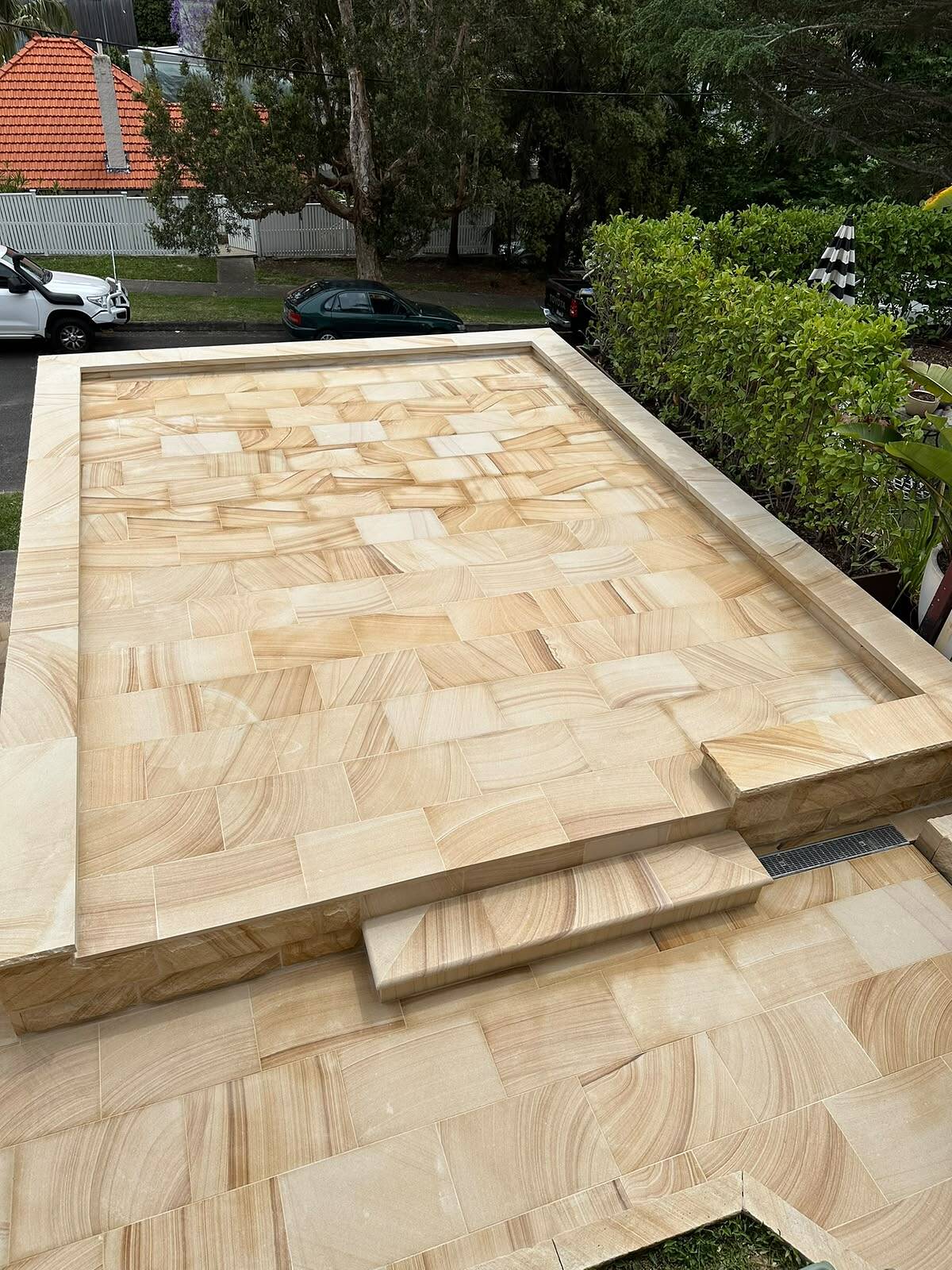 Raised front terrace paved with banded sawn sandstone flagging, coping edge and step