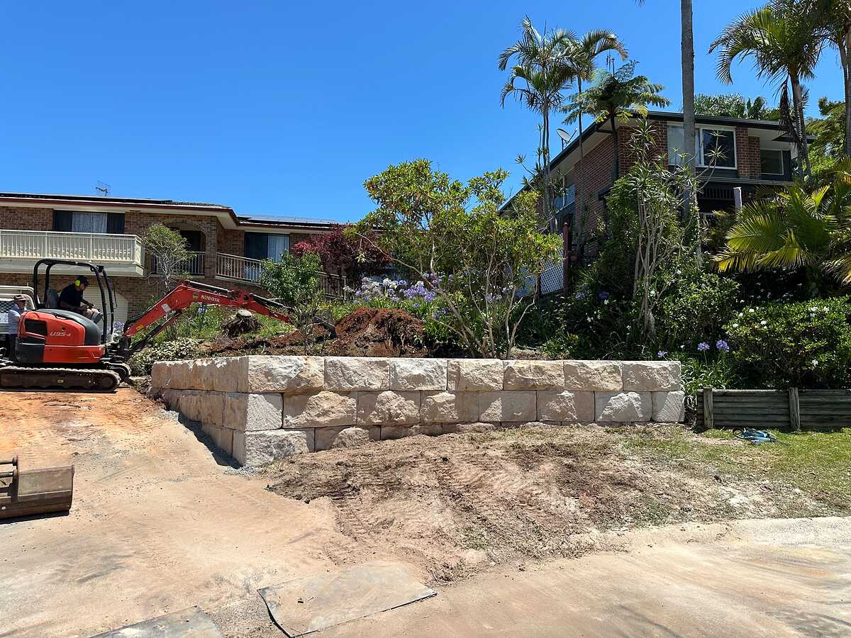 Large rock-face sandstone block retaining wall being built with an excavator on site