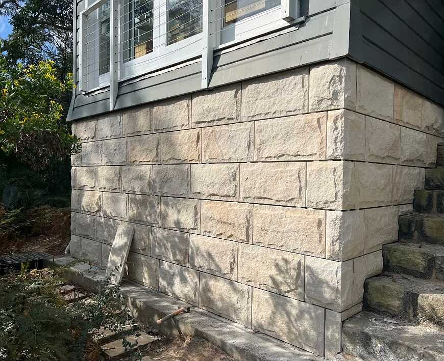 Rock-face sandstone cladding around the base of a weatherboard house beside sandstone steps