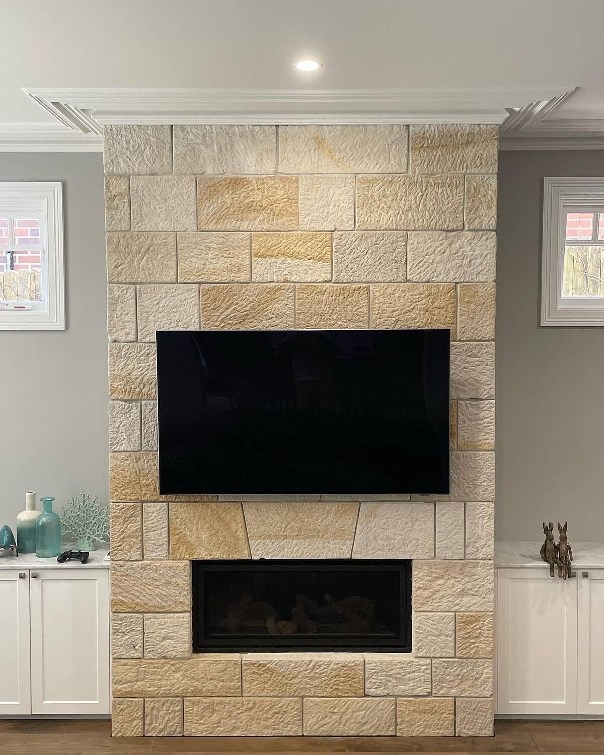 Front view of a split-face sandstone ashlar fireplace and TV feature wall between white cabinets