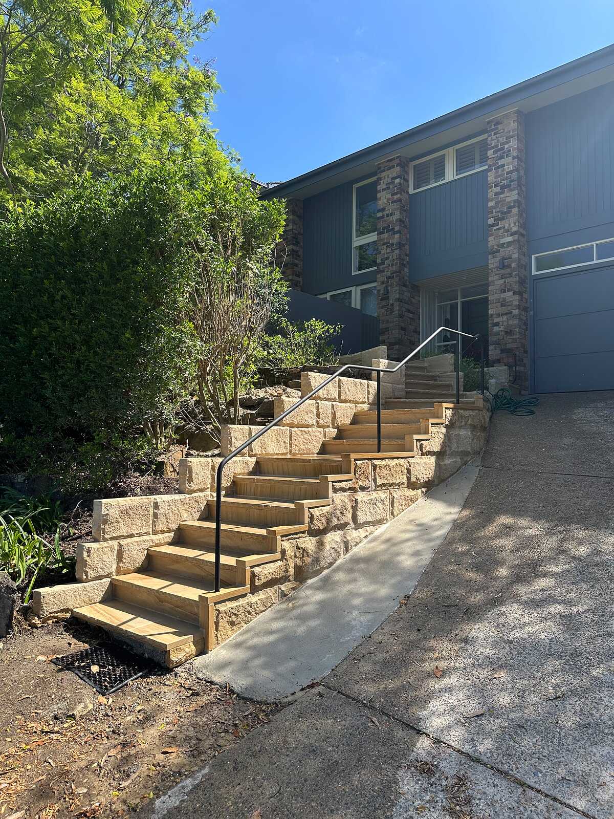 Sawn sandstone block entry steps with black handrail leading up to a blue weatherboard house