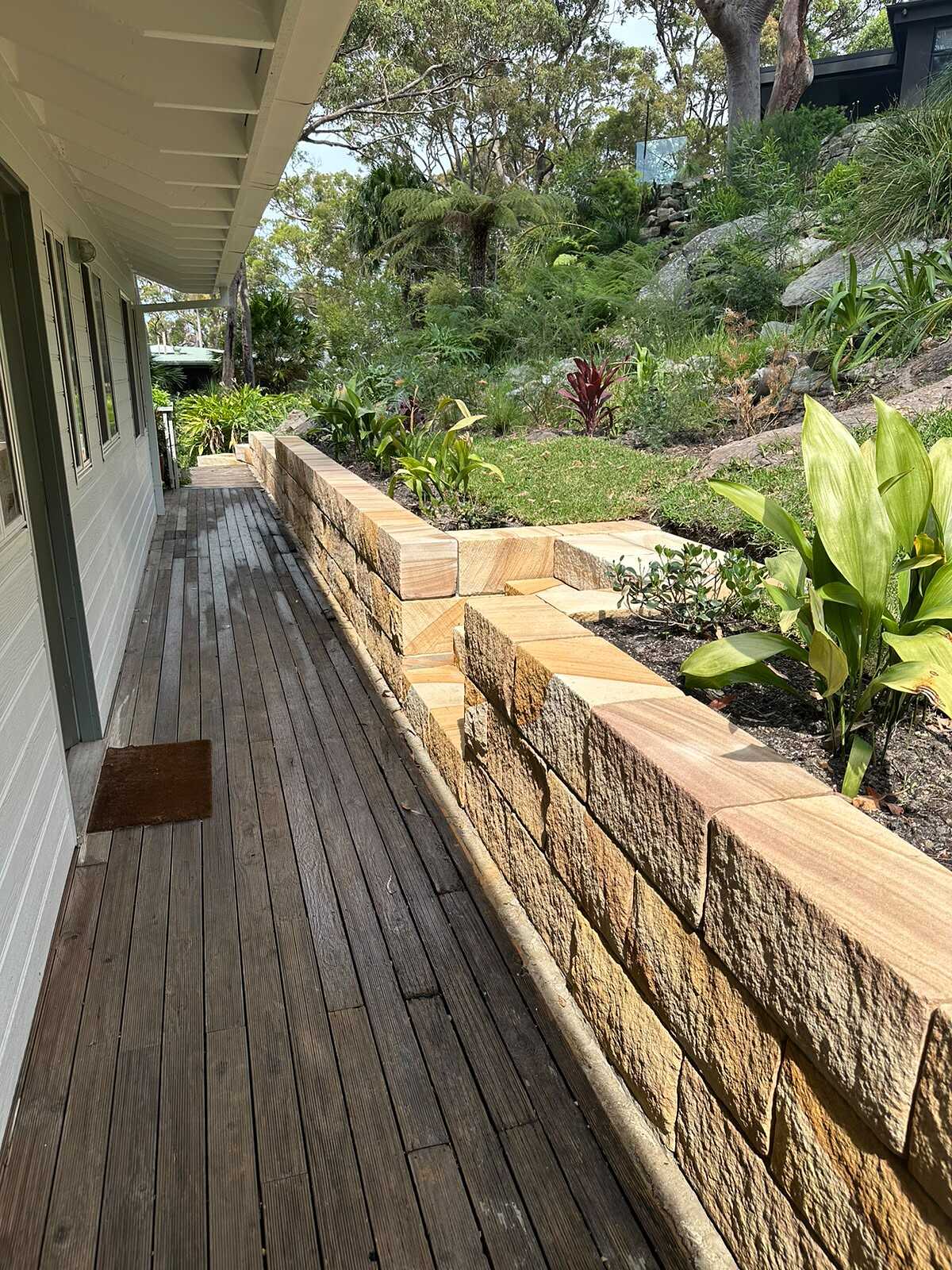 Sandstone block retaining wall with built-in steps running beside a timber veranda deck