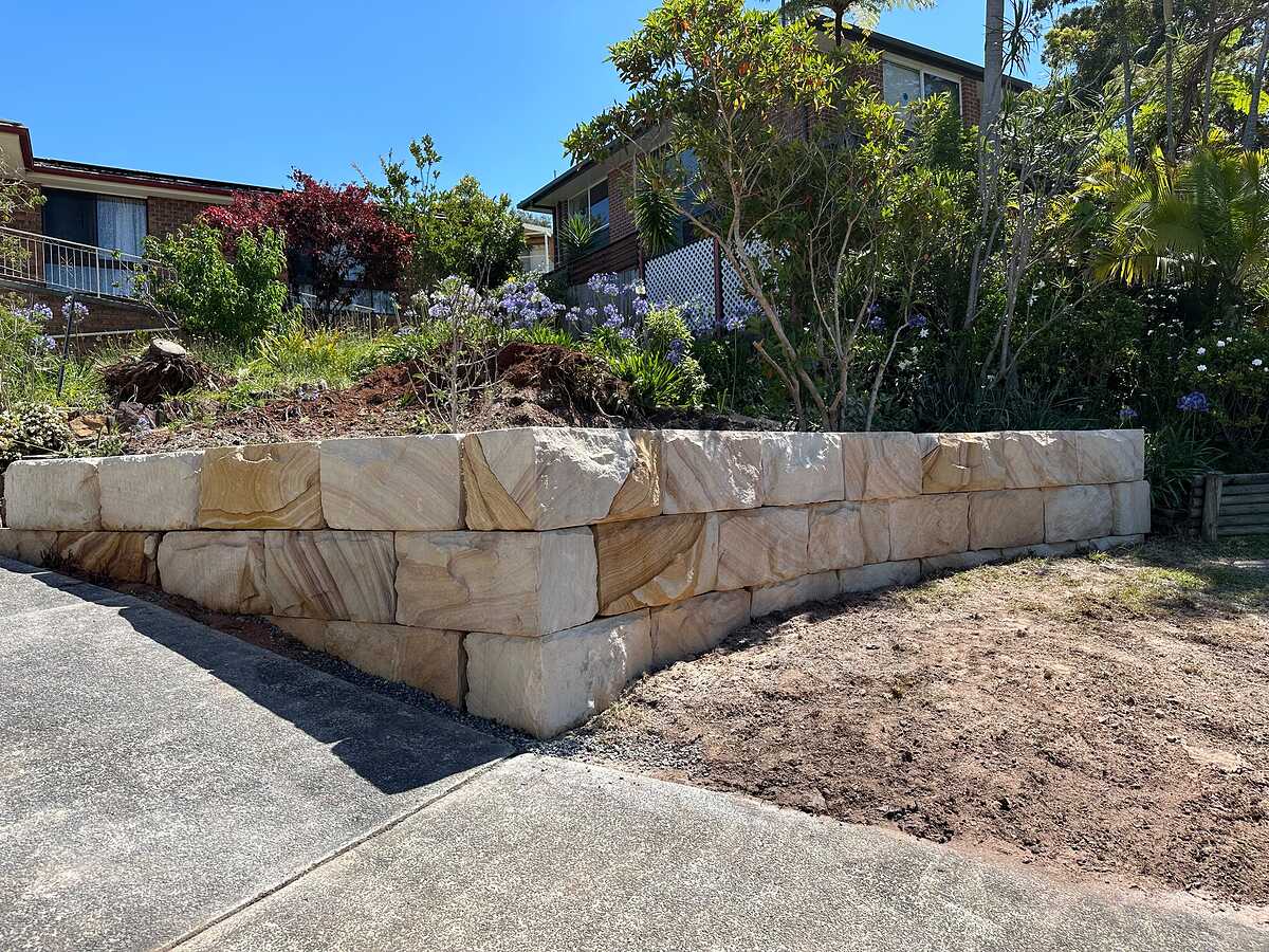 Curved sandstone block retaining wall along a sloping driveway with a planted garden above