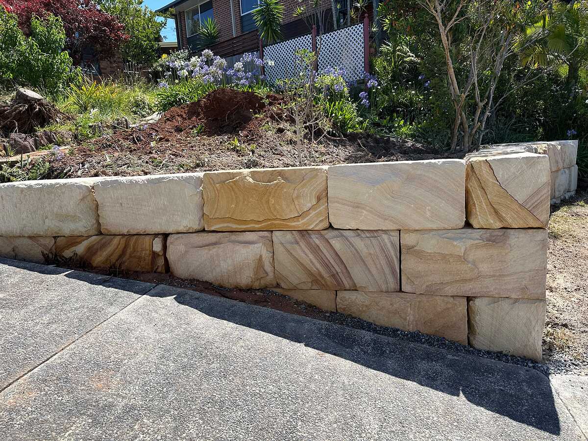 Sandstone block retaining wall stepping down beside a sloping concrete driveway