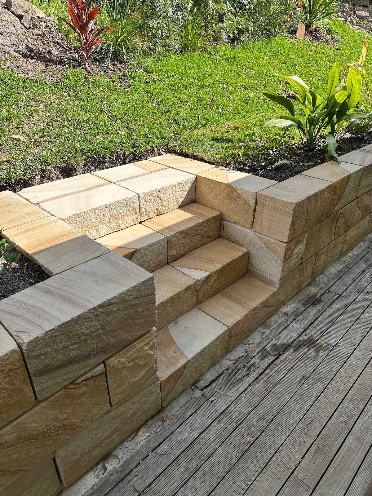 Sandstone block steps built into a retaining wall, leading from a timber deck up to the lawn
