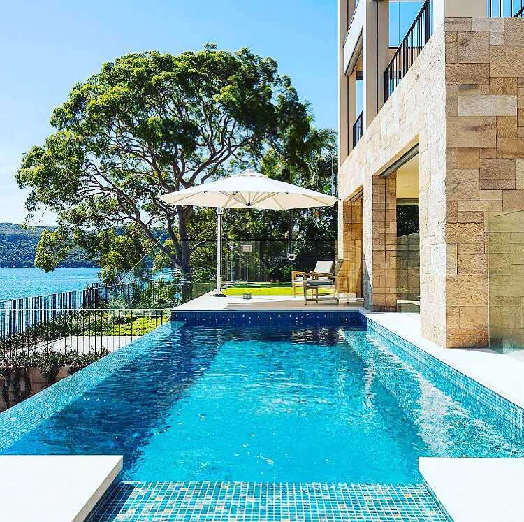 Sandstone-clad waterfront home beside a mosaic-tiled pool overlooking the water
