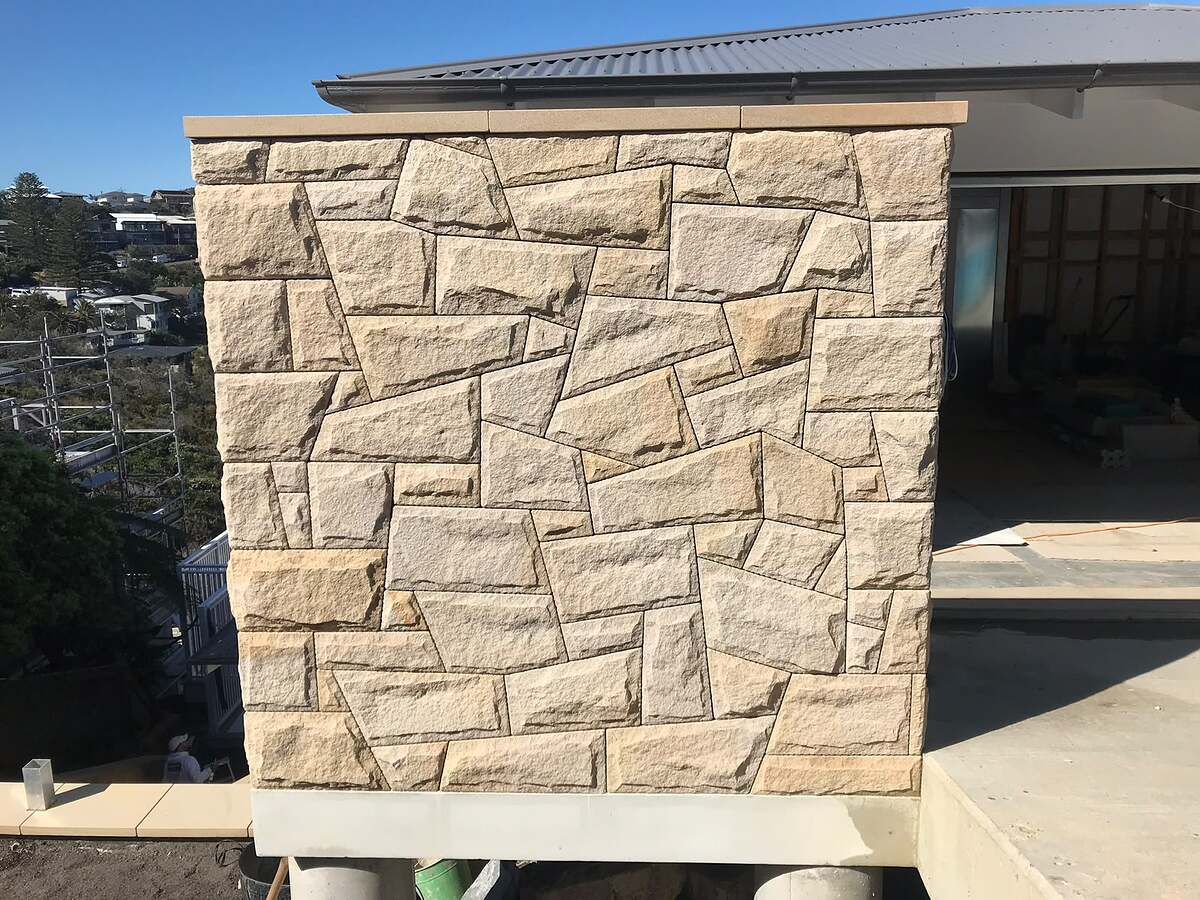 Light sandstone random ashlar cladding with sawn capping on a new home