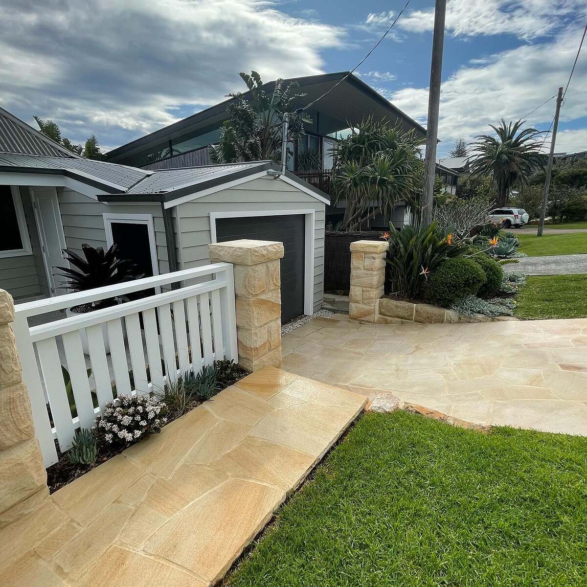 Sandstone crazy paving entry and rock-face pillars with a white picket fence