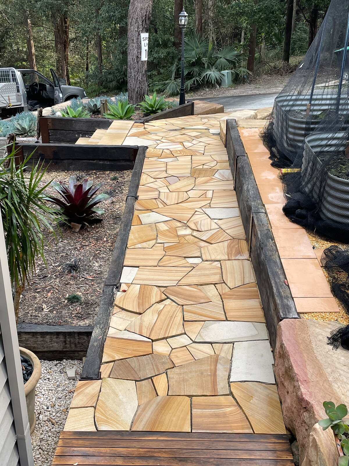 Sandstone crazy paving path between timber sleeper garden beds on a bushland block