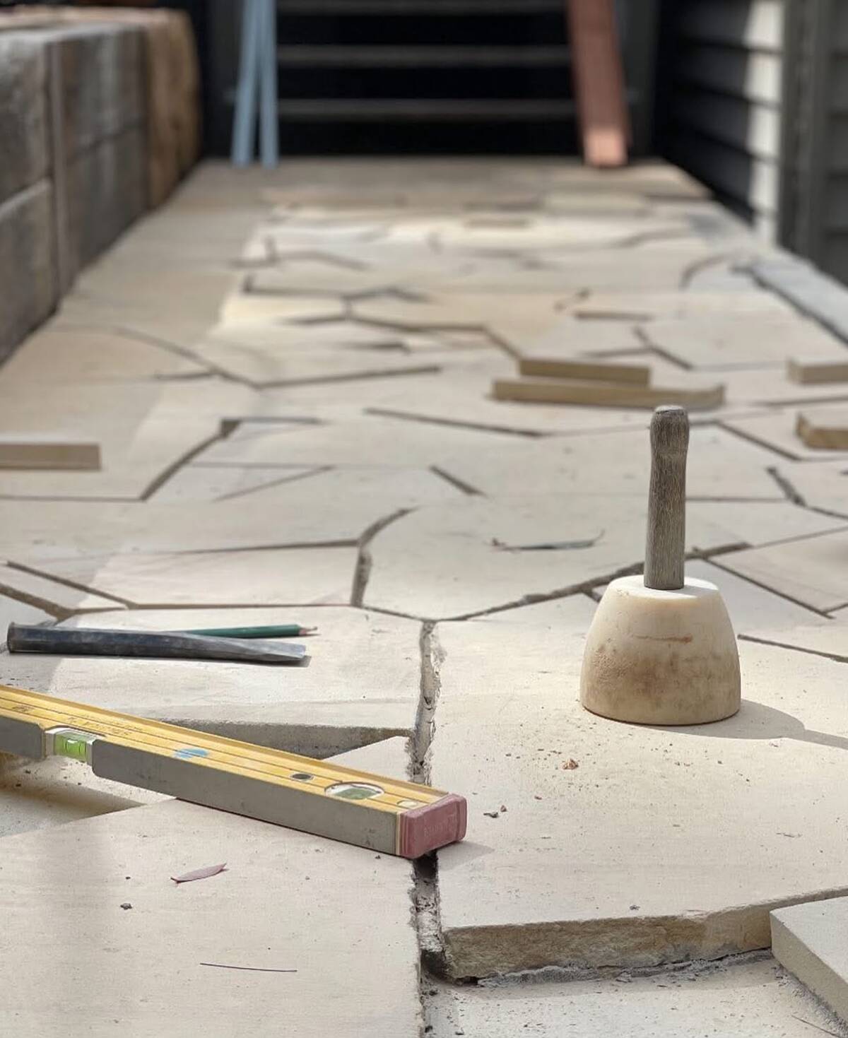 Light-coloured crazy paving being laid with a mason's mallet and spirit level