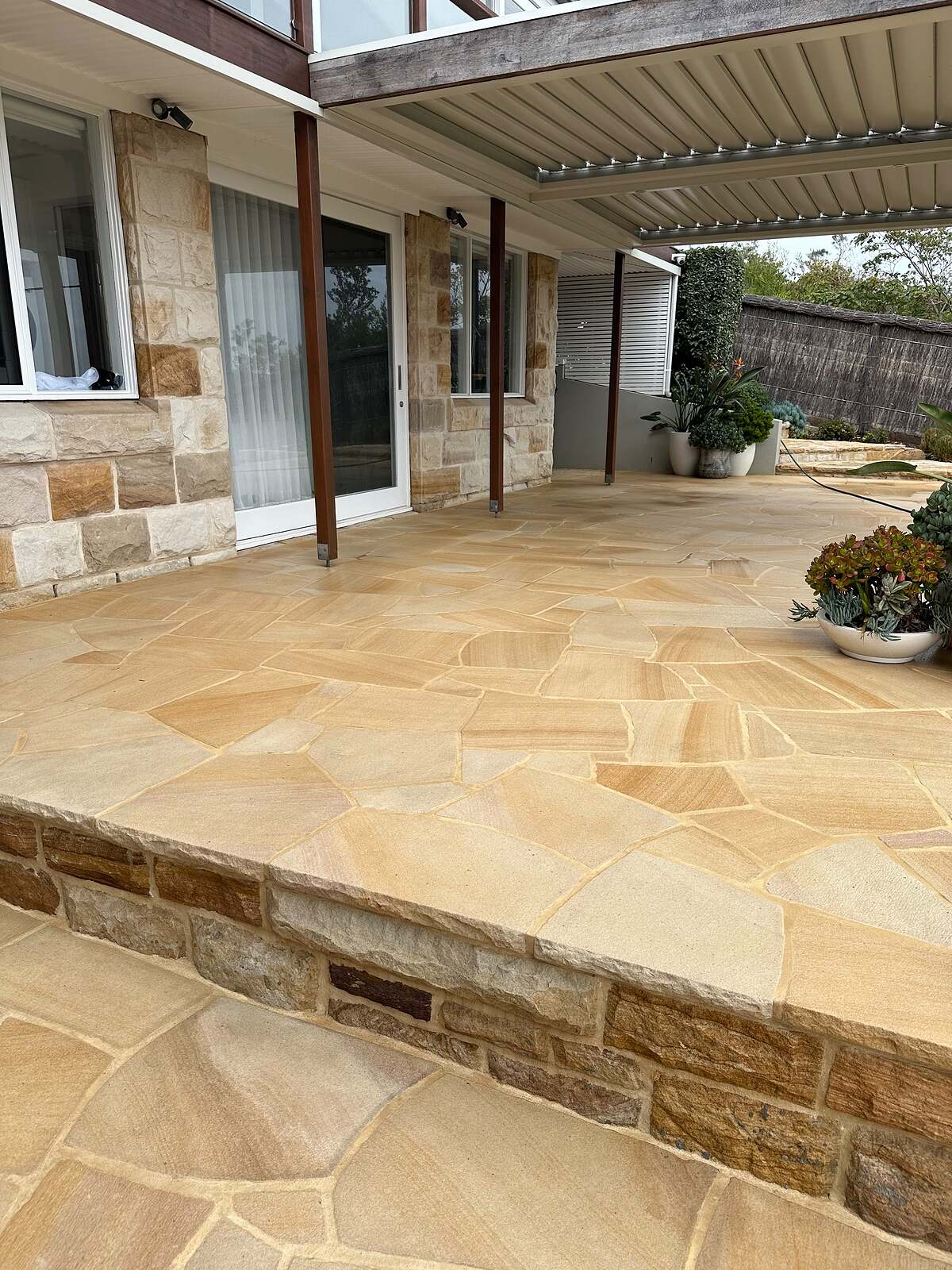 Sandstone crazy paving terrace with raised sandstone block edge outside a sandstone home