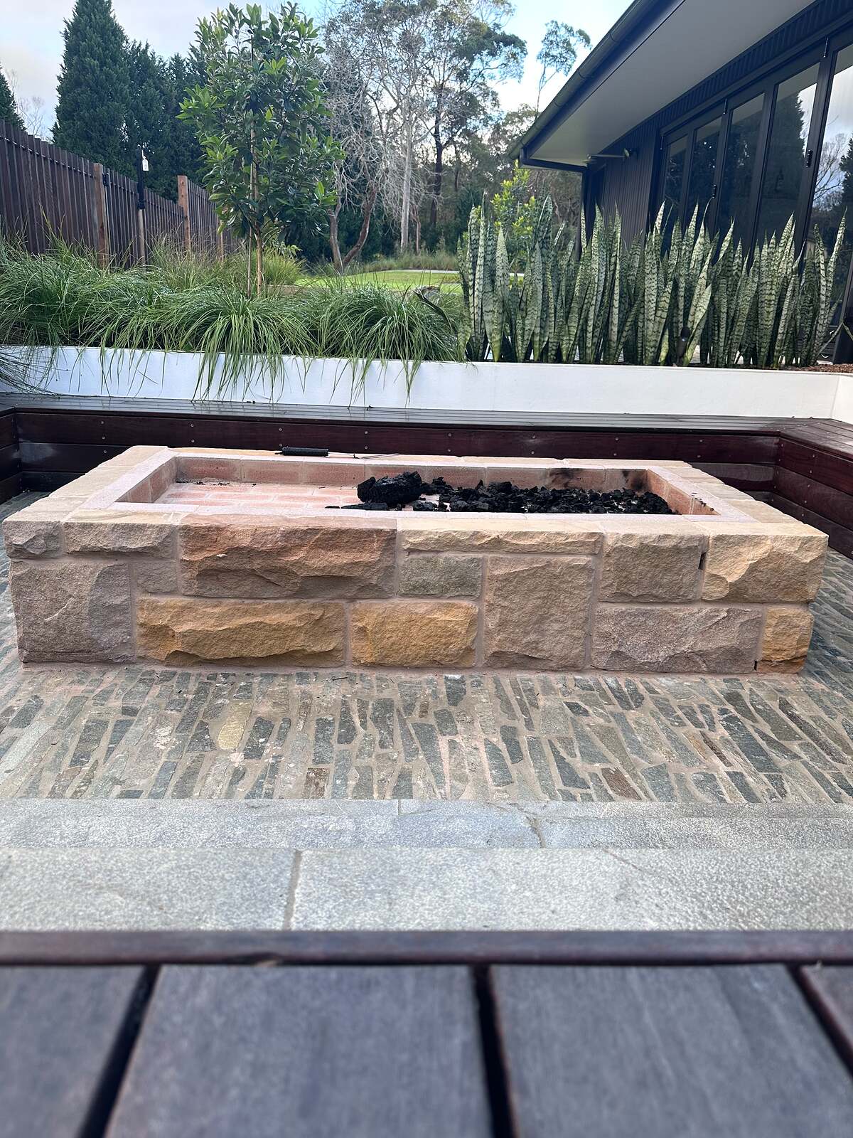 Rectangular sandstone fire pit on blue-grey stone cobble paving with built-in bench seating