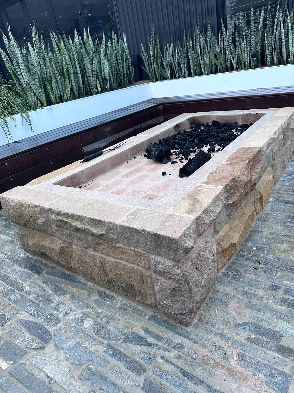 Close-up of a sandstone fire pit with split-face blocks, sawn coping and blue-grey stone cobbles