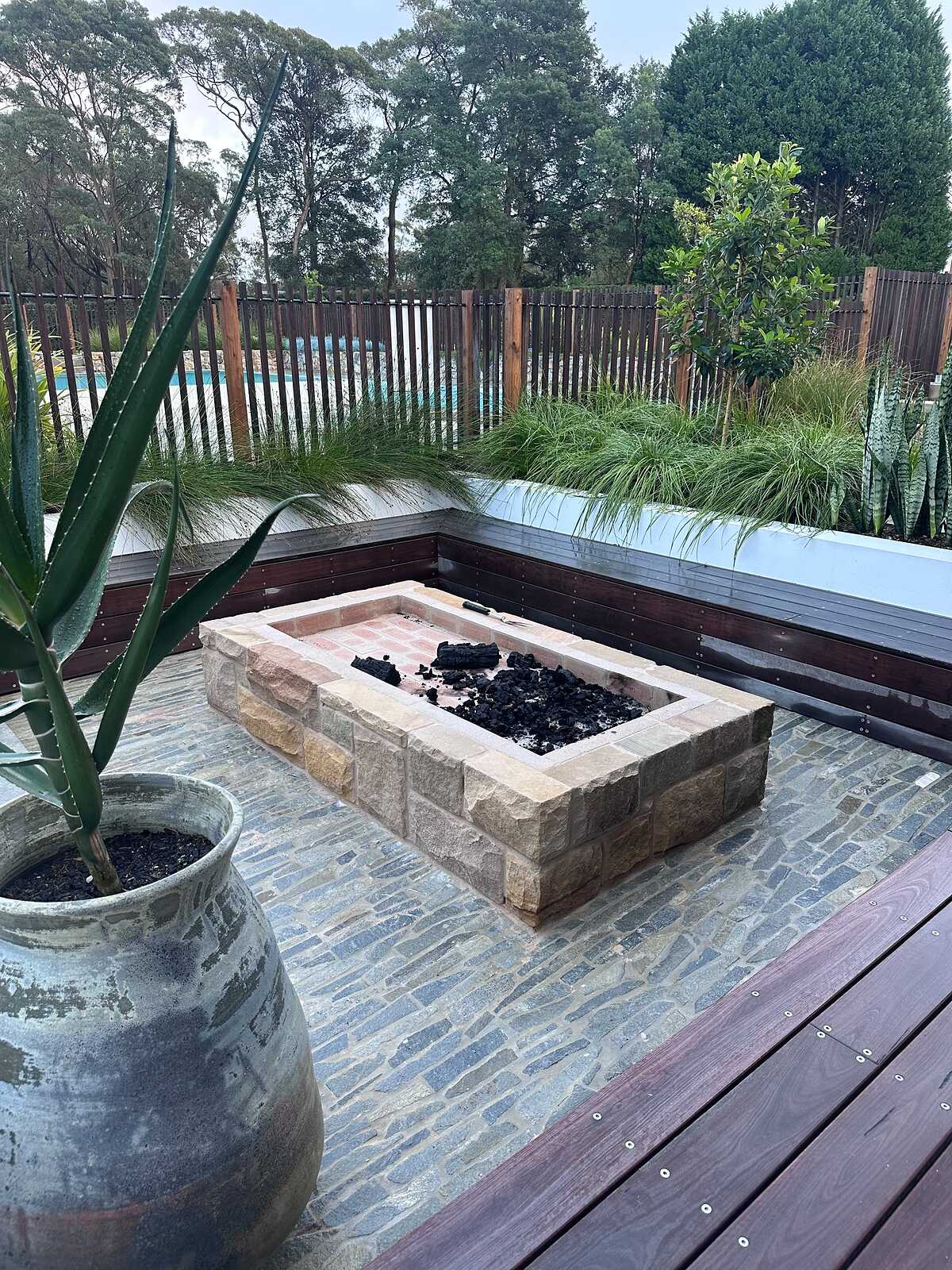 Sandstone fire pit on a blue-grey stone cobble courtyard with timber bench seating and garden