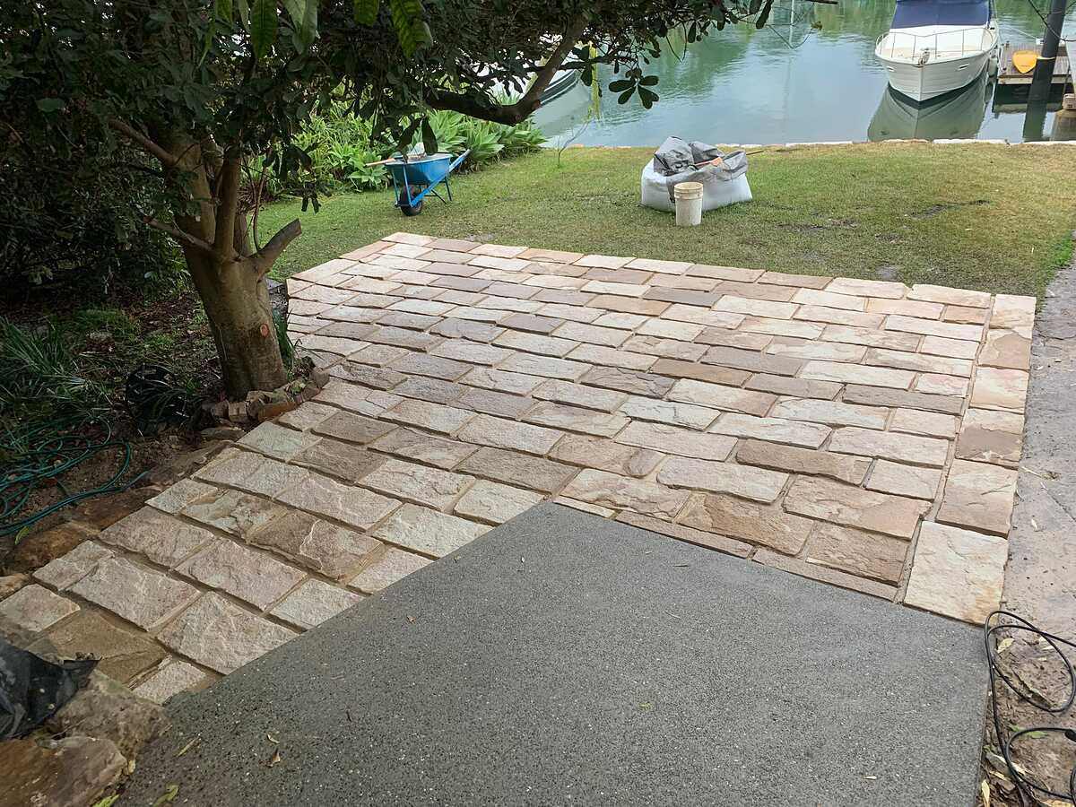 Sandstone paver patio on a waterfront lawn with boats moored behind