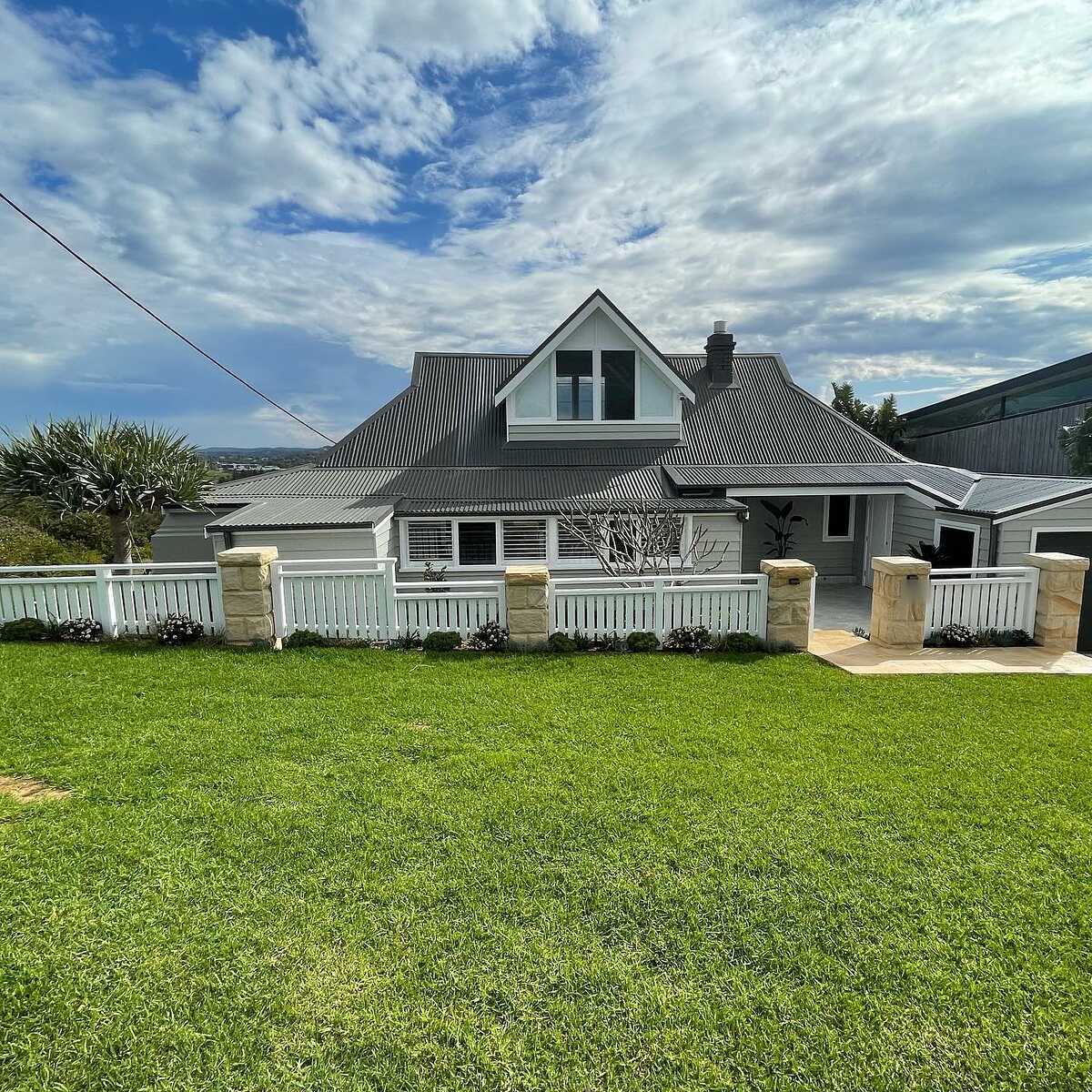 Rock-face sandstone pillars and white picket fence in front of a coastal weatherboard home