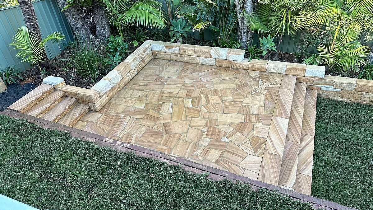 Backyard sandstone patio of random-cut flagging with low block seating walls and steps set into lawn