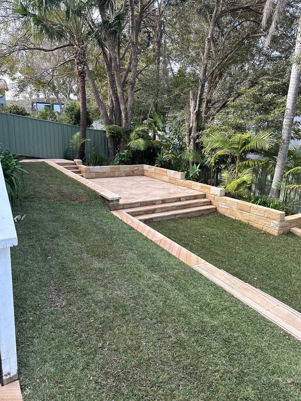 Sawn sandstone steps and paved landing with low block walls in a lawned backyard