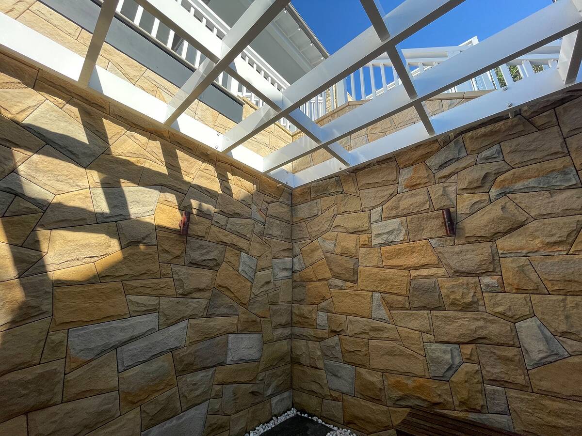 Sandstone wall cladding in a courtyard under a white pergola with bronze wall lights