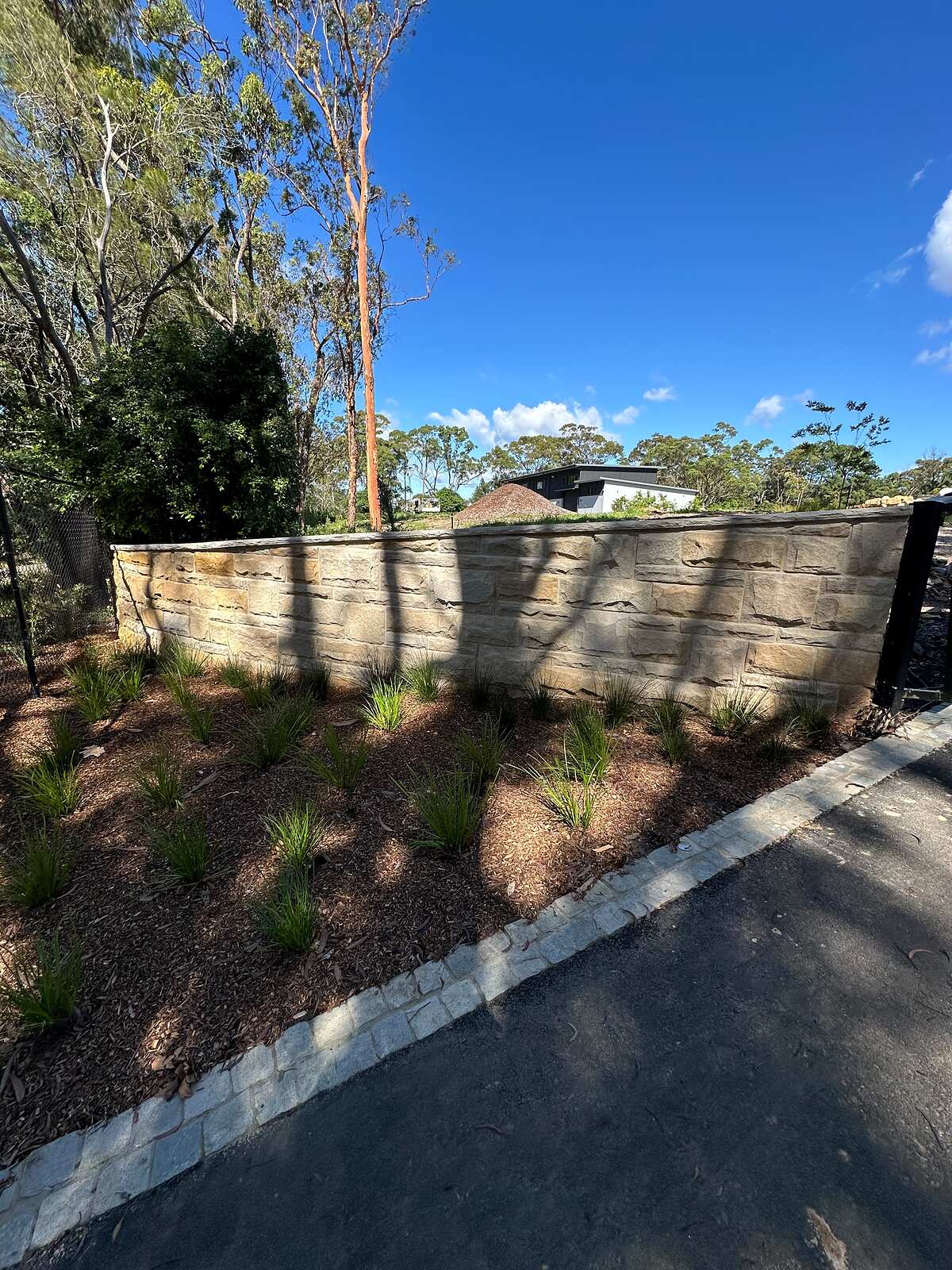 Long sawn sandstone block wall beside a bushland driveway with stone sett edging