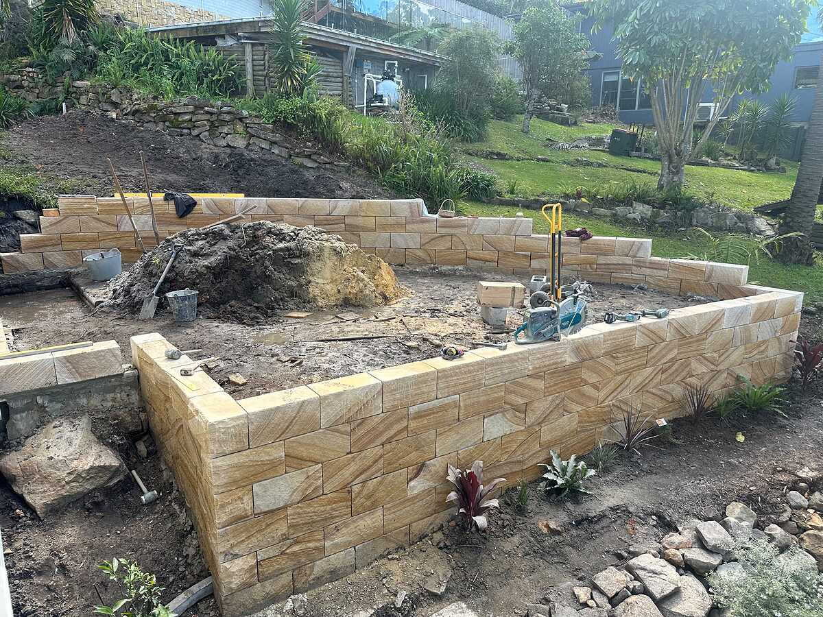 Sawn sandstone block garden walls being built to terrace a sloping backyard