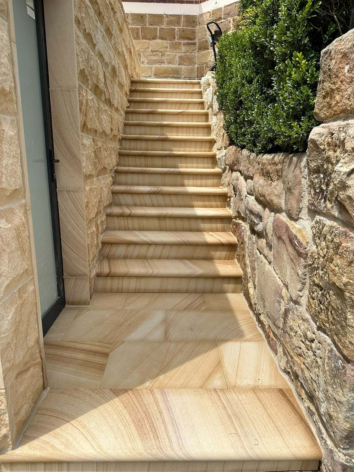 Sawn sandstone staircase in a side passage between split-face cladding and a rubble sandstone wall