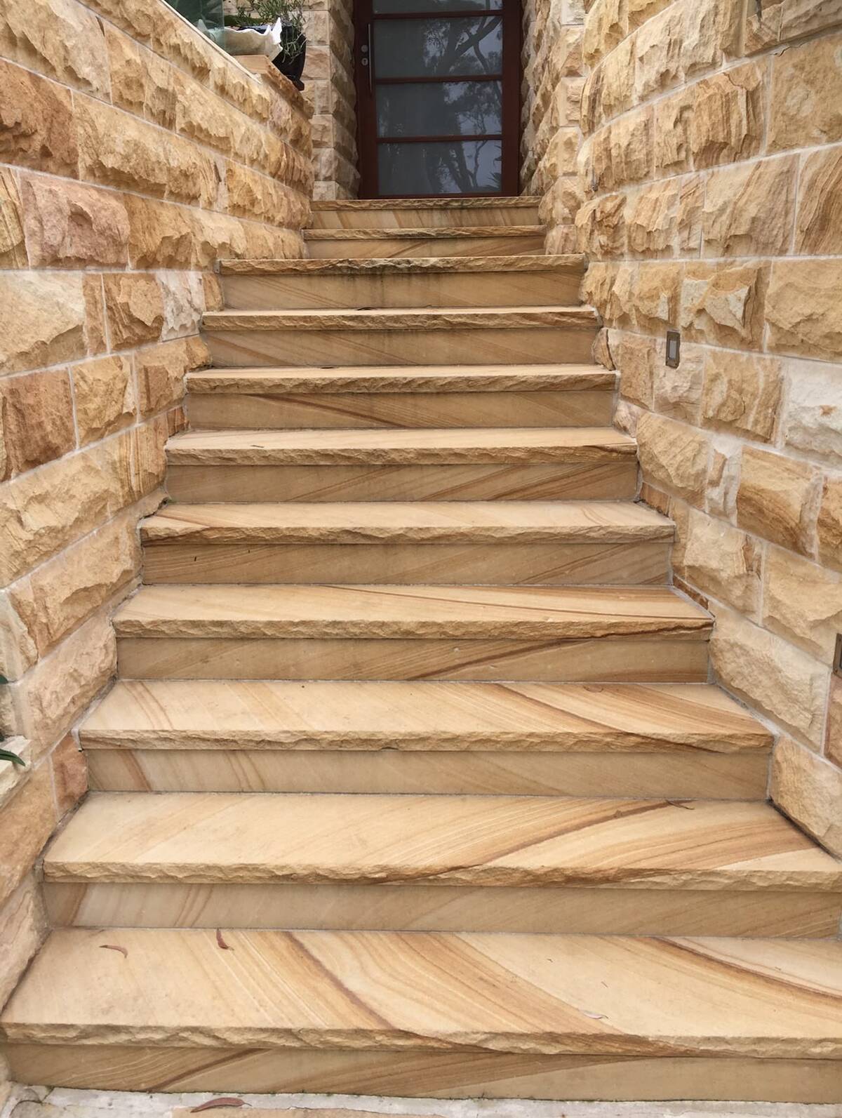 Sawn sandstone stairs between split-face sandstone walls leading to a timber door