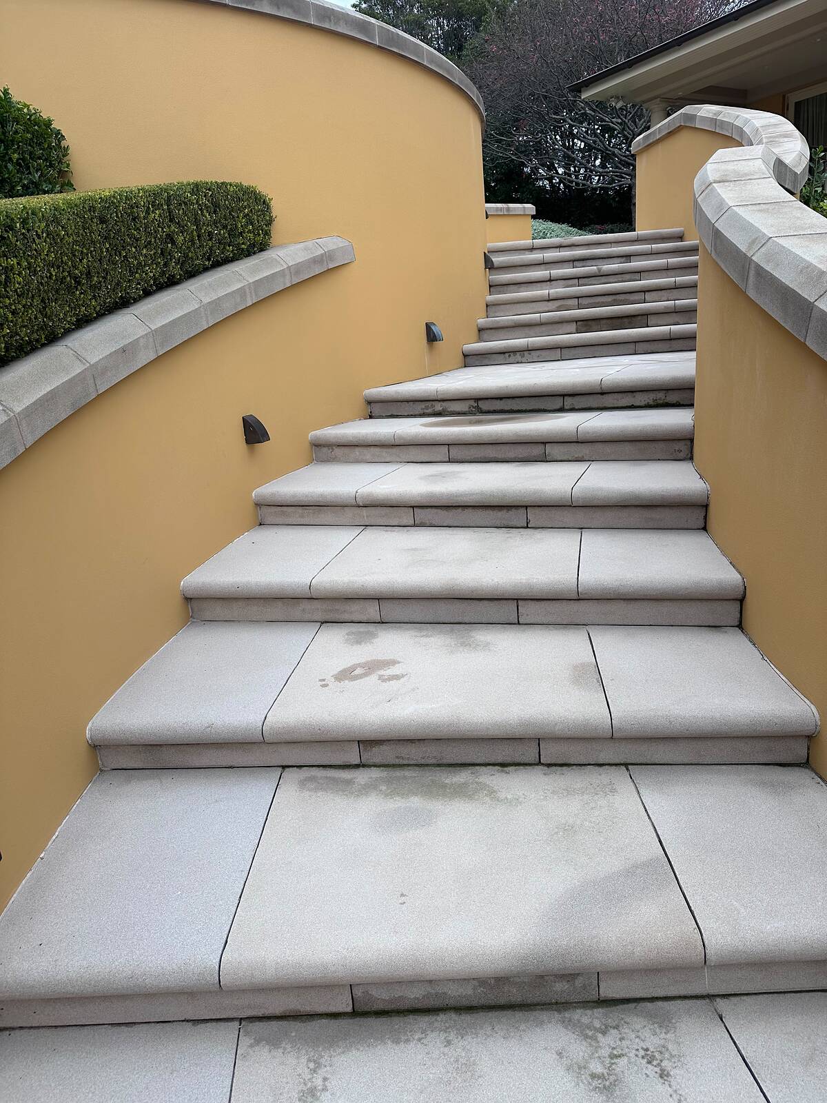 Sawn sandstone stair treads climbing between curved rendered walls with sandstone coping