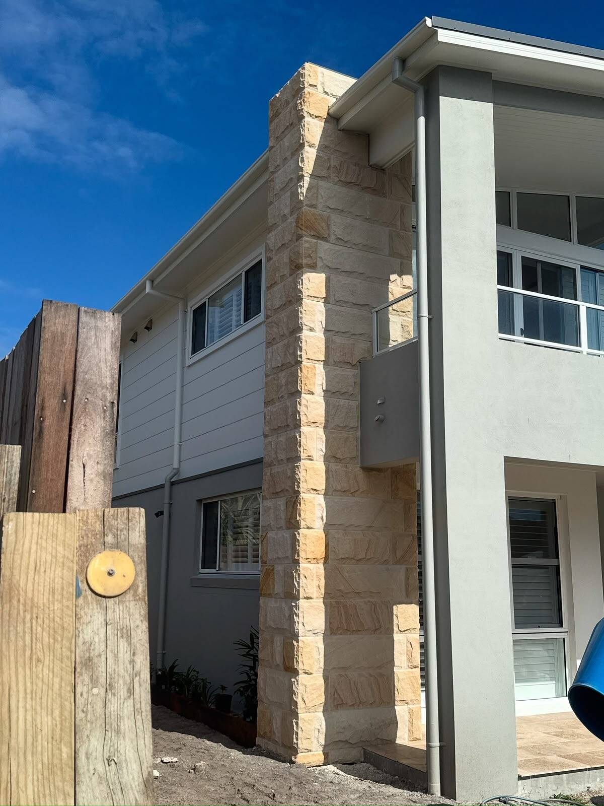 Split-face sandstone cladding on a tall entry pier of a modern grey two-storey home