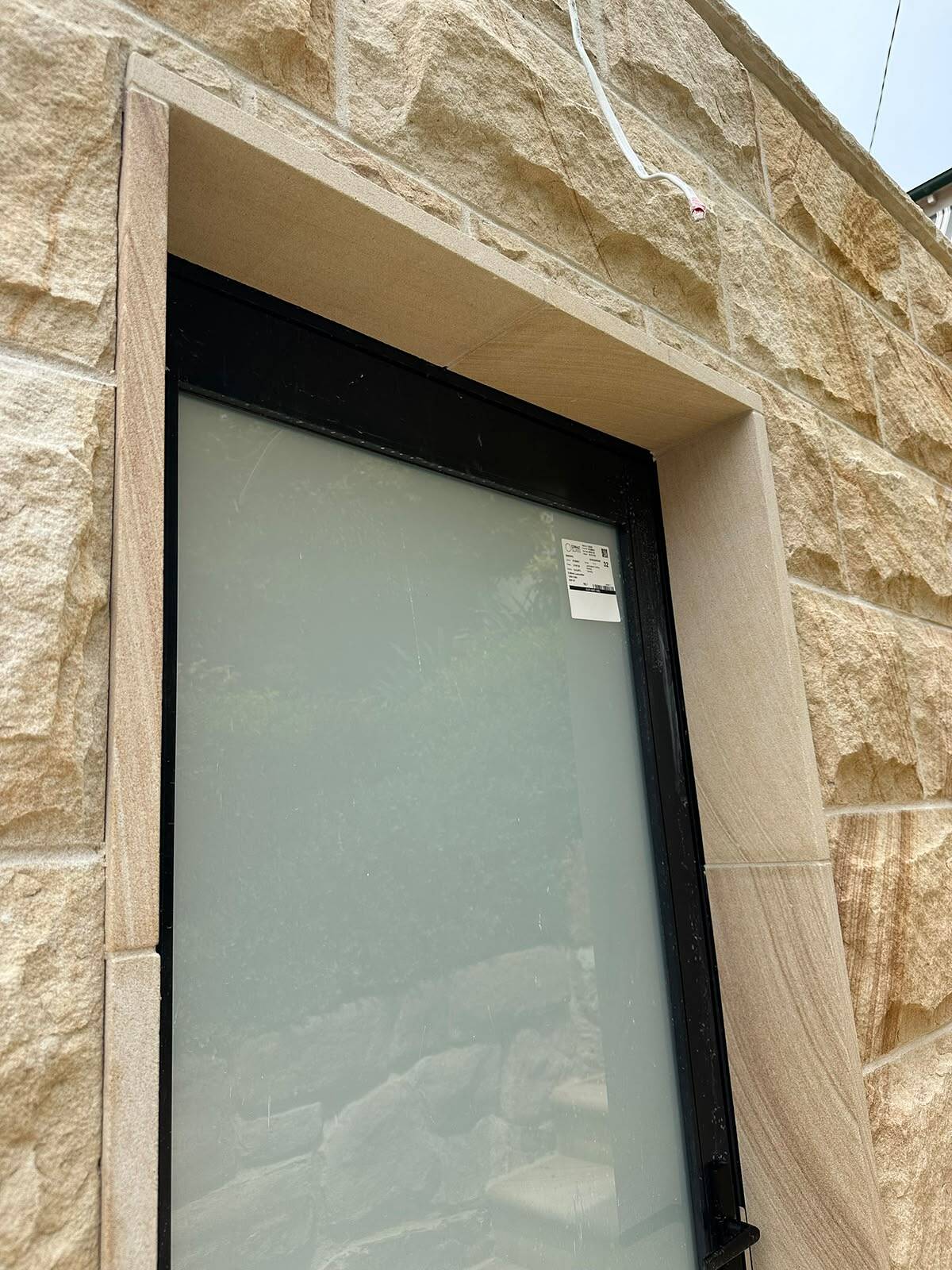 Sawn sandstone window reveal set into split-face sandstone ashlar cladding