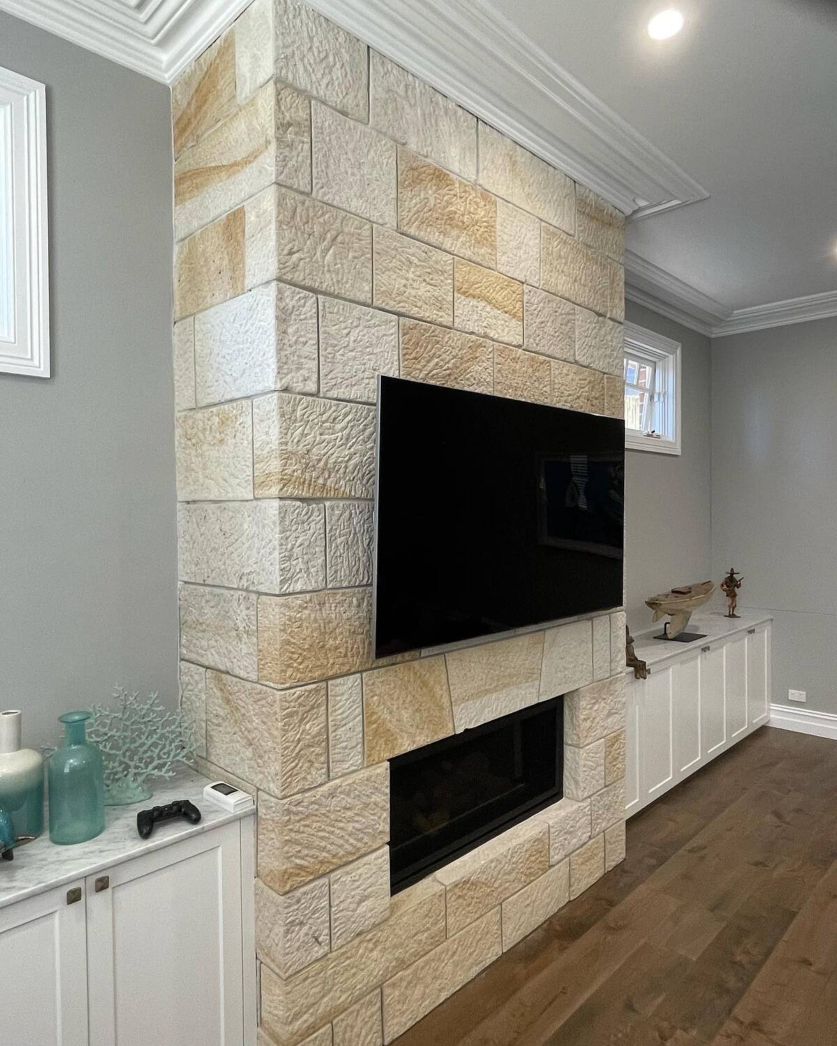 Split-face sandstone ashlar fireplace wall with TV above a linear gas fire in a bright living room