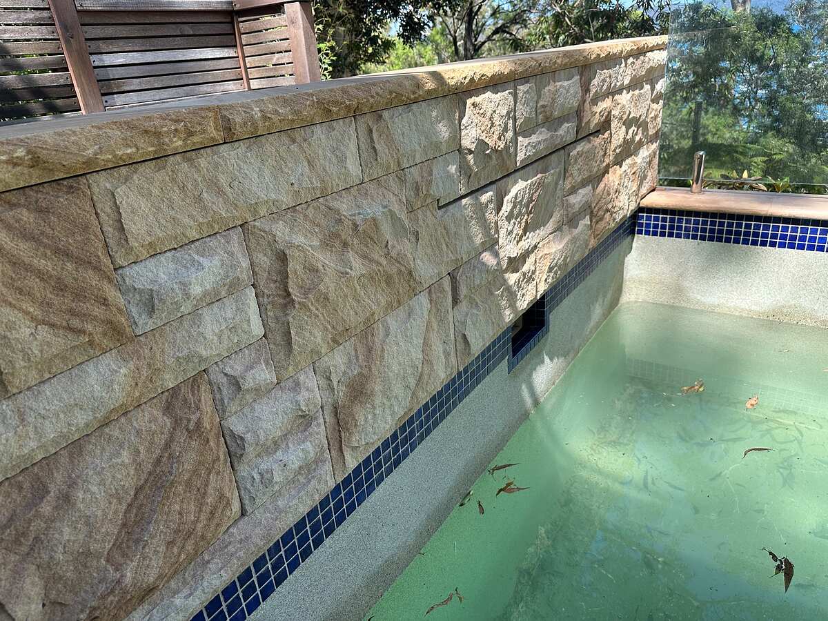 Close-up of split-face sandstone pool wall with sandstone coping and blue waterline tiles