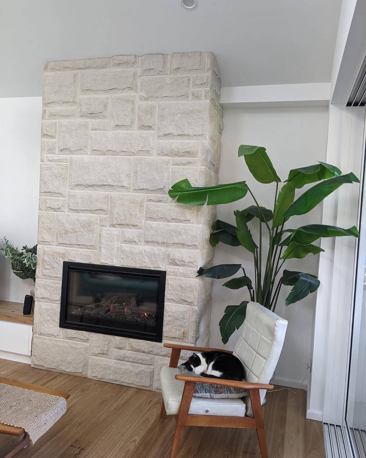 White rock-face natural stone fireplace with linear gas fire beside an indoor plant